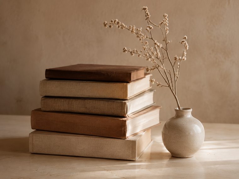 A stack of books beside a vase of dried stems